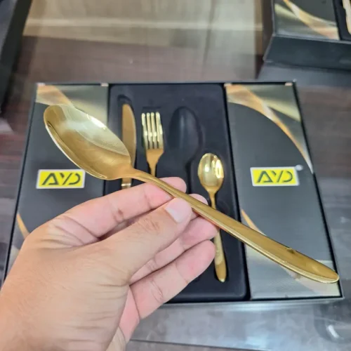 AVD 24-Piece Gold Cutlery Set - Held in Hand Hand holding AVD gold spoon from 24-piece cutlery set